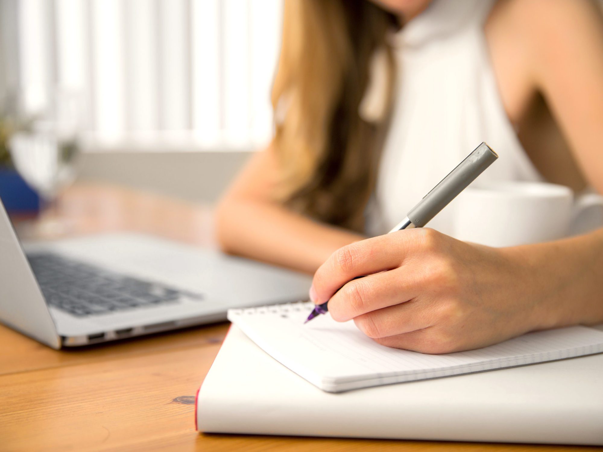 Hand pen coffee cup laptop table close up bokeh background taking notes Close-up of hand writing secretary executive business person personal assistant student